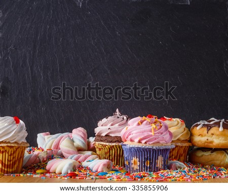 Sweets with copy space on black slate background. Donuts and cupcakes