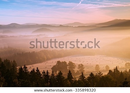 Pink daybreak in fall hilly countryside. Autumn misty morning in a beautiful hills. Peaks of hills are sticking out from fog