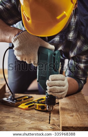 Craftsman in helmet and gloves holding drill at work. Male contractor woodworking with building tools.  Royalty-Free Stock Photo #335968388