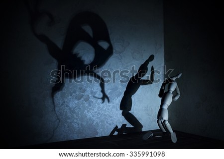Background with shadow games. Wooden manikin is hiding in a corner and fear rose up in its heart because of horrible monster has appeared .Image with selective focus and toning
