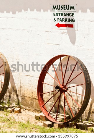 Old rusted metal wheel under sign on wall at entrance to agricultural museum 