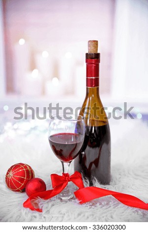 Bottle and glass of wine with Christmas decor against colorful bokeh lights background 