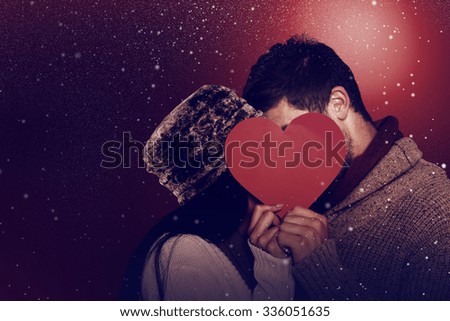 Young couple kissing behind red heart against snow