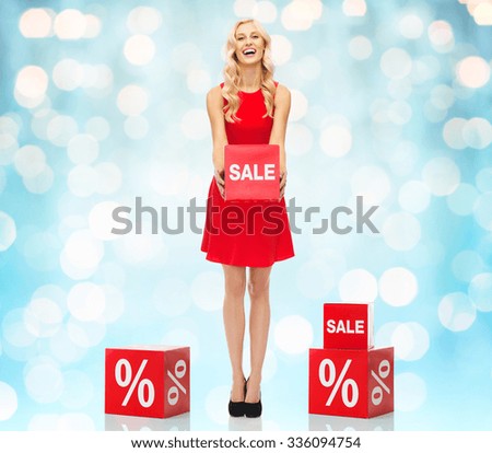 people, shopping, discount and holidays concept - smiling woman in red dress holding cardboard box with sale sign over blue holidays lights background