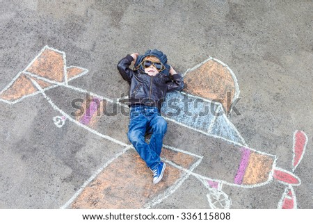 Funny little kid boy flying by a plane picture painting with colorful chalk. Creative leisure for children outdoors in summer.
