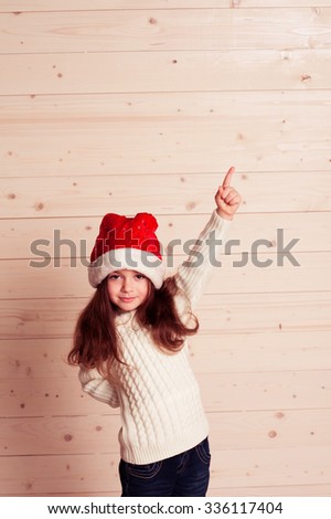 Kid girl 4-5 year old wearing christmas hat showing by finger up. Looking at camera. Smiling child. 