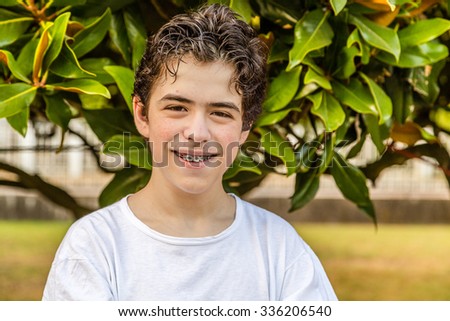 teenager with acne skin smiling while showing braces with green magnolia tree in the background