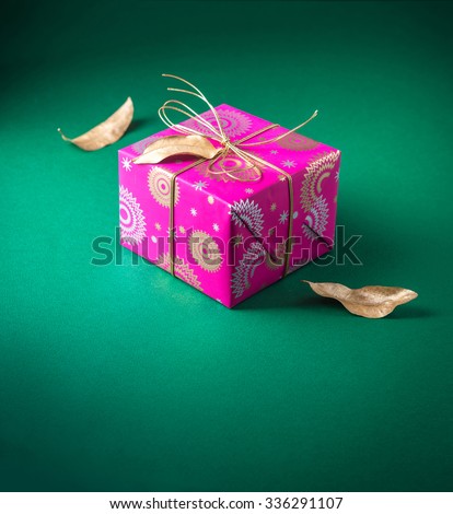 Beautiful small gift box wrapped with bright pink wrapping paper and arranged with dry golden leaves. Festive object and background.