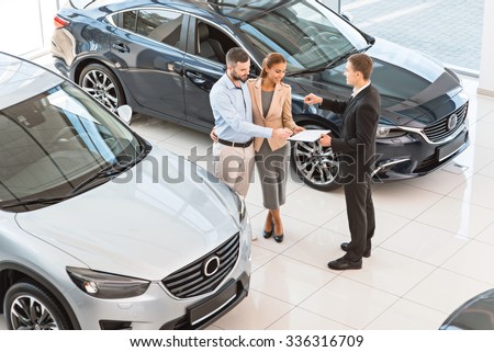 Top view photo of young male consultant and buyers signing contract for new car in auto show. Concept for car rental