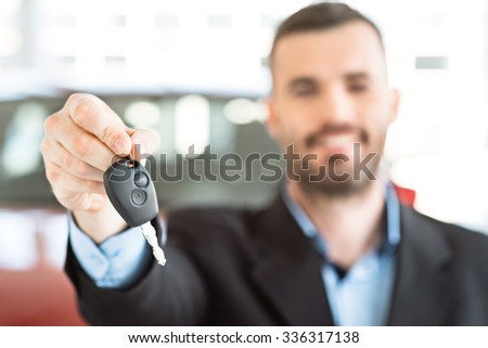 Photo of happy young man showing key to his new car. Concept for car rental. Focus on key