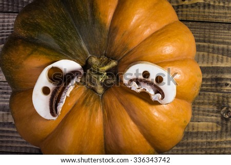 Top view closeup rotary photo still life one big whole fresh orange pumpkin with two slices of champignon with cut Halloween ghost faces on wooden table on timber background, horizontal picture 