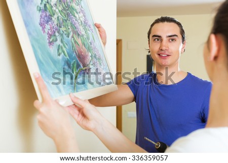 Young man and woman hanging art picture in frame