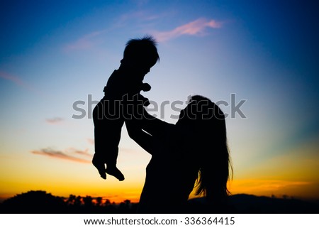 a silhouette picture of mother holding her baby while the sunset and twilight sky.