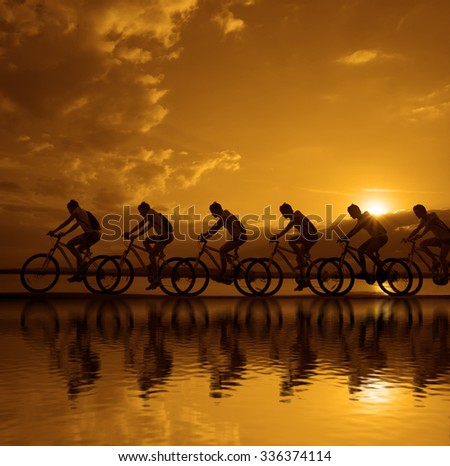 Image of sporty company friends on bicycles outdoors against sunset. Silhouette A lot phases of motion of a single cyclist along the shoreline coast Reflection on water Space for inscription