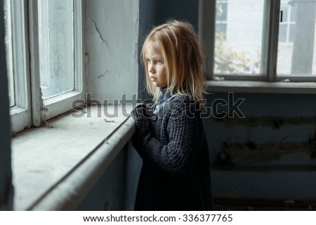 Hopeless life. Close up of depressed poor little girl standing near window and looking aside while feeling miserable Royalty-Free Stock Photo #336377765