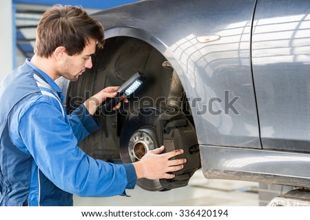 Male mechanic holding flashlight while examining brake disc of car in garage Royalty-Free Stock Photo #336420194
