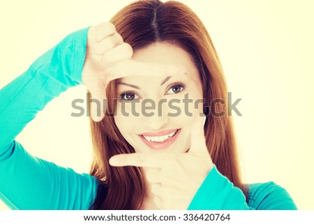 Smiling woman wearing blue blouse is showing frame by hands. Happy girl with face in frame of palms.