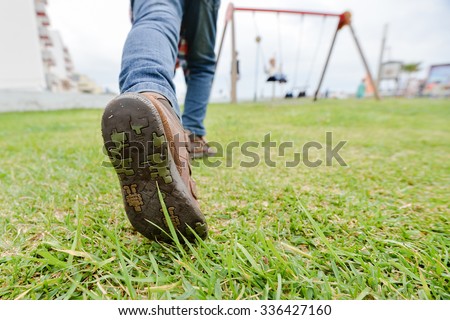 Picture of exciting boy running on children playground. Closeup of leg and boot sole on green grass outdoor background.