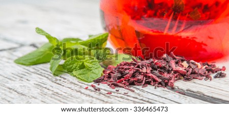 A cup of hibiscus tea and fresh mint leaves on wooden background