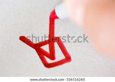 Hand with red pen marking a check box