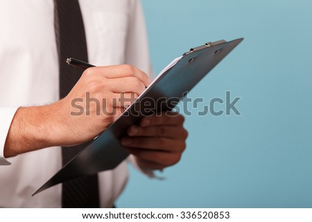 Close up of hands of a businessman holding a folder of papers and writing. The man is standing in formalwear. Isolated on blue background and copy space in right side