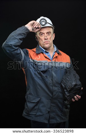 Coal miner showing lump of coal with thumbs up against a dark 