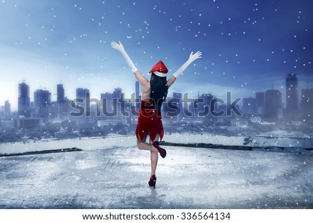 Asian woman wearing santa claus costume, standing on the rooftop, looking the city