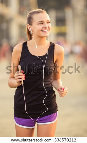The young beautiful girl with headphones running and doing fitness in city