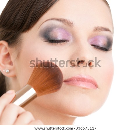 Woman applying cosmetics to her face with cosmetic brush, isolated on white