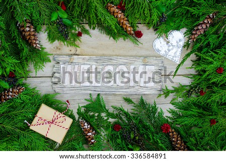 Welcome sign with brown paper package tied up in string, silver tin heart and green Christmas tree garland border on antique rustic wood background