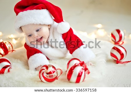 
Happy Smiling baby lying on tummy wearing a red and white Christmas Santa hat and suit, isolated on a white background.