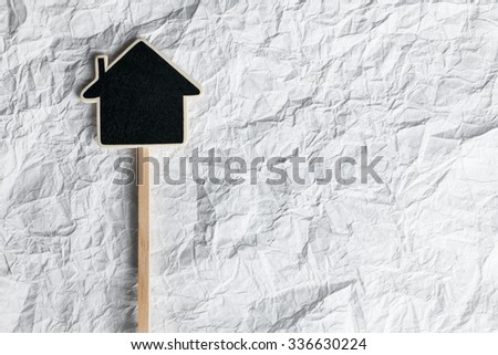 Wooden pointer in the shape of a house lying on a crumpled paper, as background