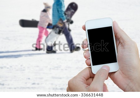 Man holding smart phone, tablet over blurred skiers in the background, winter background.