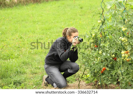 Girl kneeling on grass and taking close-up photo of tomato plant with copyspace on left side of photo