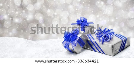 Silver Christmas or birthday gift boxes with red bows in snow, with snowy night background, panorama format