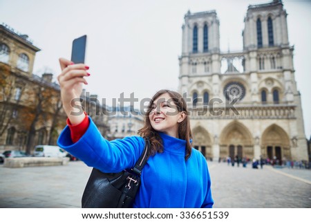 Beautiful young tourist in Paris on a fall day, making selfie with Notre-Dame cathedral