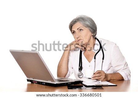 Thoughtful senior doctor sitting at table with laptop