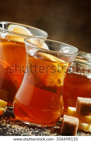 Black hot tea with honey, lemon and cane brown sugar in Middle Eastern glasses on a dark background, toned image, selective focus