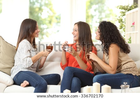 Three happy friends talking and drinking coffee and tea sitting on a couch at home Royalty-Free Stock Photo #336702170