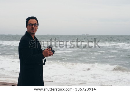 handsome hipster photographer traveler tourist guy wearing glasses and hat taking photo of hazy cold sea with his film camera 