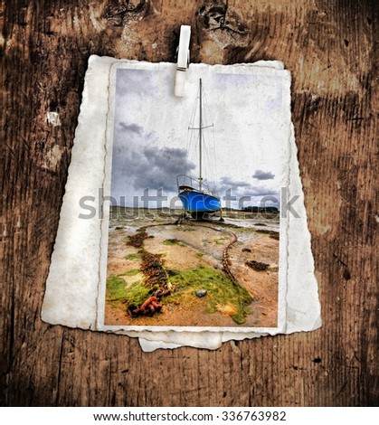 pile of old vintage photographs on a wooden background with on top a colorful image from  a old boat in the distance with a big chain at low tide on shore

