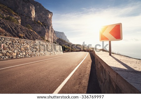 Asphalt road in autumn forest at sunrise and road sign. Crimean mountains.