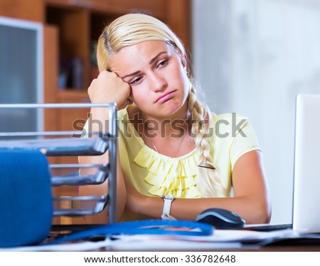 Tired young girl sitting at desk with laptop in office