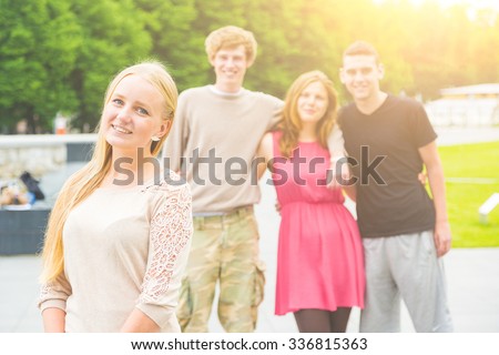 Portrait of a blonde young woman with a small group of friends on background. She is in her early twenties, smiling and looking at camera. Multiethnic group. Friendship and lifestyle concepts.