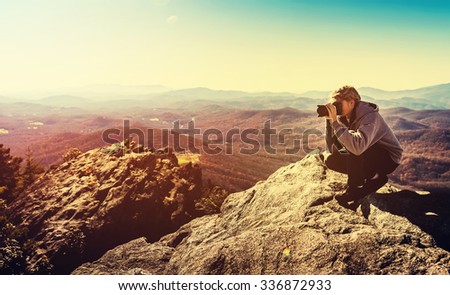 Man with a camera at the edge of a cliff overlooking the mountains below