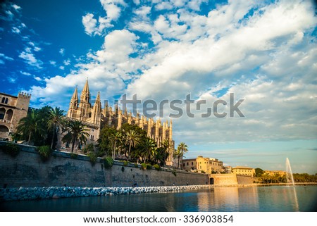Cathedral of Palma de Mallorca with plam trees and water reflections of the pool against blue cloudy sky. Big gothic church on the sea shore. Beautiful travel picture of Spain.