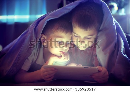 Two kids using tablet pc under blanket at night. Brothers with tablet computer in a dark room Royalty-Free Stock Photo #336928517