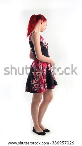 full length portrait of a pretty red haired girl wearing thick glasses and a cute flower print dress, side view. smiling and looking at the camera. Isolated on white background.
