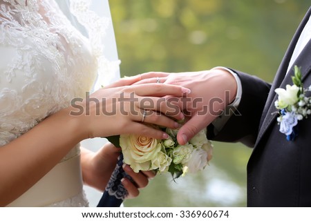Closeup view of wedding young beautiful tender couple holding hands changing golden engagement rings with rose flowers bouquet outdoor, horizontal picture