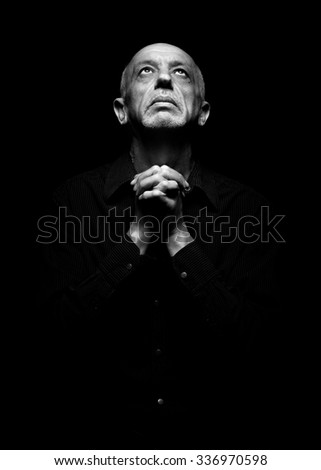 Senior man praying looking up with folded hands in the dark
